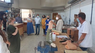 Telpā cilvēki stāv, skatās un klausās, ko rāda un stāsta sieviete, kas tur rokās ortozes sagatavi