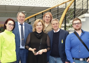 Kopbilde, kurā redzama SIVA direktore I.Jurševska, Rehabilitācijas pakalpojumu nodaļas vadītāja Ludmila Jefimova un ergoterapeite Diāna Čunčule kopā ar trīs vīriešiem stāv pie kāpnēm. 