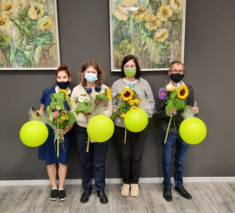 Četri ESF projekta absolventi stāv un tur rokās ziedus un balonus