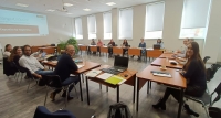 Plašā telpā sēž cilvēki pie galdiem