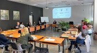 Plašā telpā sēž cilvēki pie galdiem
