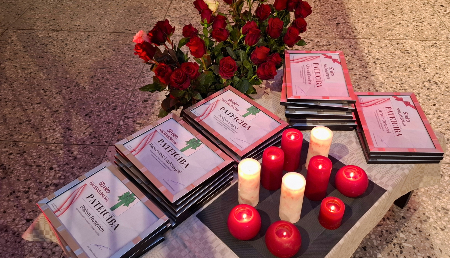 Sarkanbaltsarkanas sveces un ziedi novietoti blakus ierāmētām pateicībām