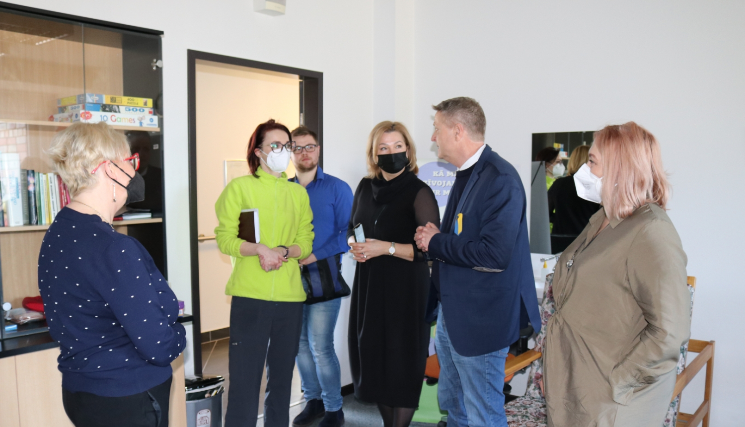 Viesi un SIVA darbinieces stāv psihologa nodarbību telpā un sarunājas.