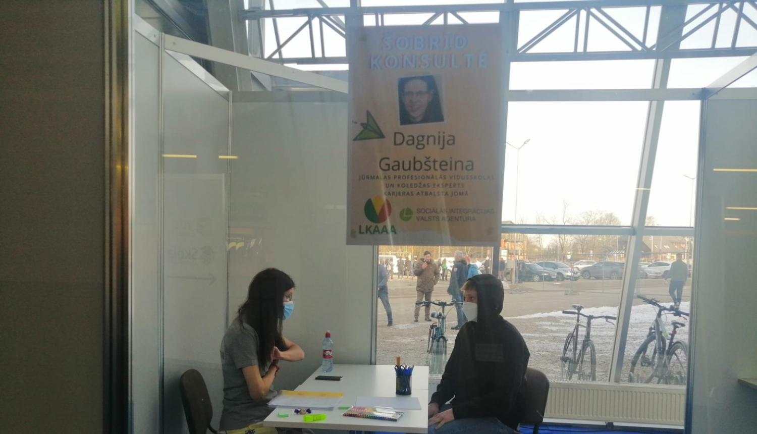 Pie balta galda sēž SIVA karjeras konsultante un skolēns. SIVA darbiniece sarunājas ar skolnieku.