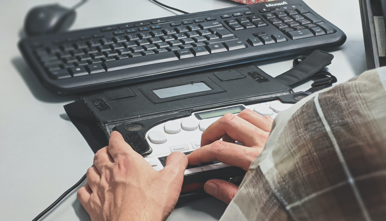 Cilvēks pie galda izmanto pielāgoto datora tastatūru