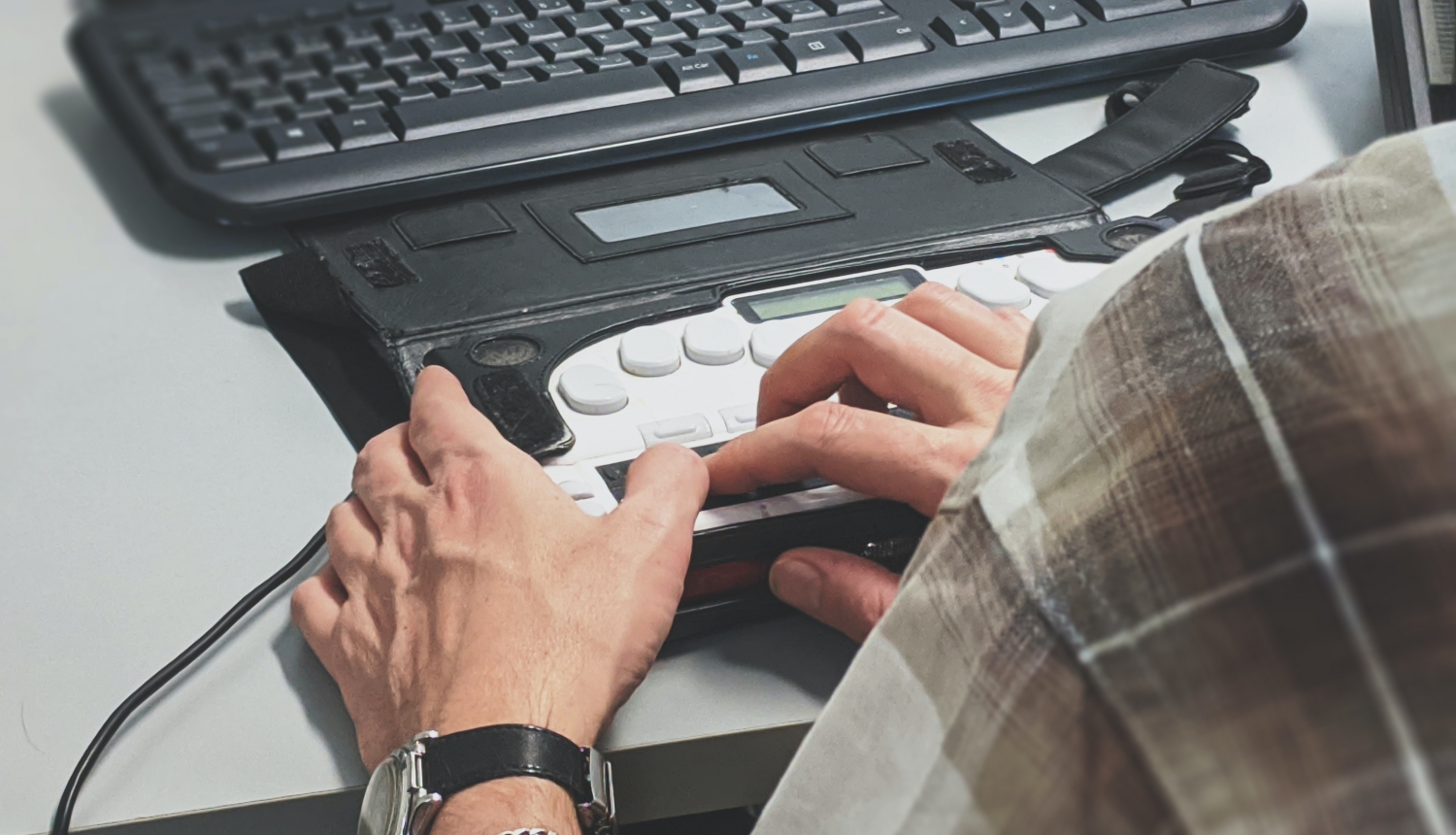 Cilvēks pie galda izmanto pielāgoto datora tastatūru